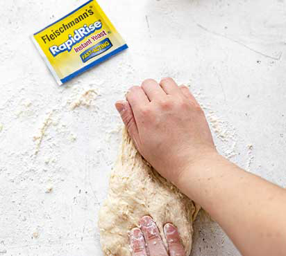 Two hands kneading dough next to a packet of Fleischmann's yeast